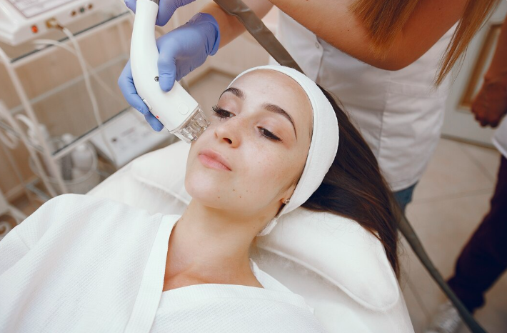 A practitioner in blue gloves performing a gentle microneedling treatment on a woman's cheek in a clinical setting, illustrating acne scar treatment for sensitive skin