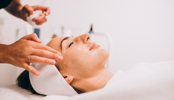 Woman lying relaxed with eyes closed while a practitioner applies a clear rejuvenating serum to her face during a professional anti-aging facial skin tightening treatment in Dubai