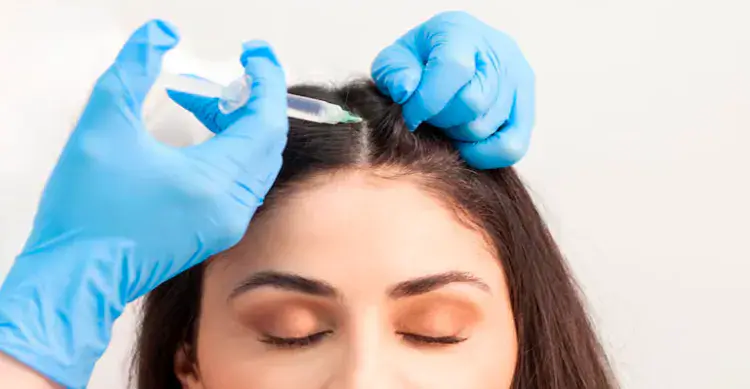 A medical professional wearing blue gloves administering a hair mesotherapy injection into a female patient's scalp to treat hair loss and promote hair growth in Dubai - Dr. Elham Keikha