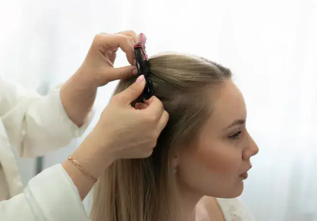 Medical professional in a white coat sectioning a patient's hair with clips to examine the scalp during a hair restoration consultation in Dubai