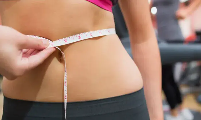 A close-up of a person measuring their waist with a tape measure in a gym, illustrating non-surgical fat reduction body contouring in Dubai