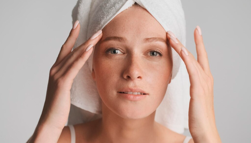 Woman with a white head towel examining facial freckles and pigmentation spots on her forehead and cheeks during a skincare routine