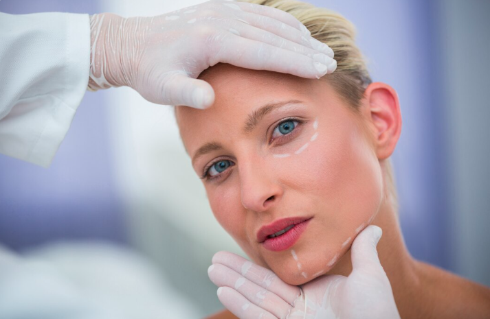 Close-up of a woman's face with white surgical markings along the jawline and under-eye area during a professional skin assessment by a practitioner in white medical gloves at a Dubai aesthetic clinic