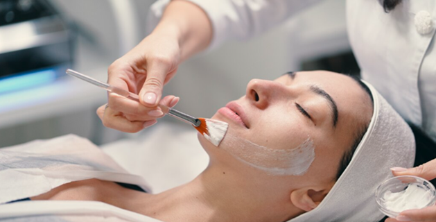 Close-up of a woman with clear, healthy skin holding delicate speckled flower petals to her cheeks, representing targeted skincare for melasma and pigmentation