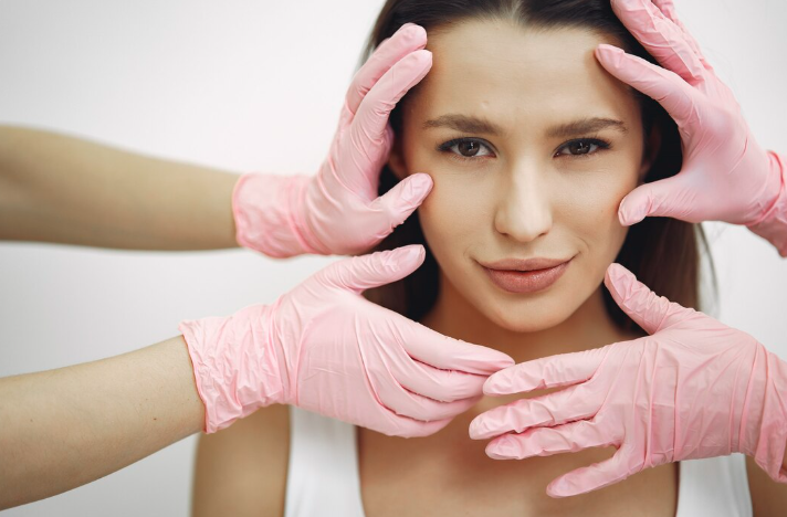 Woman's face being gently assessed by a practitioner wearing pink medical gloves during a clinical evaluation for skin tightening candidacy in Dubai