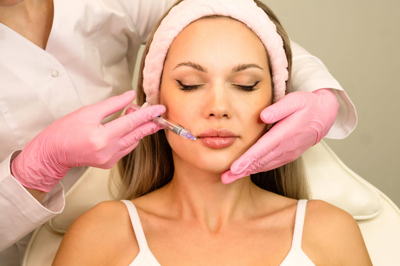 A specialist in pink medical gloves performs a precise dermal filler injection on a patient's nasolabial folds, demonstrating professional technique in a sterile Dubai clinic