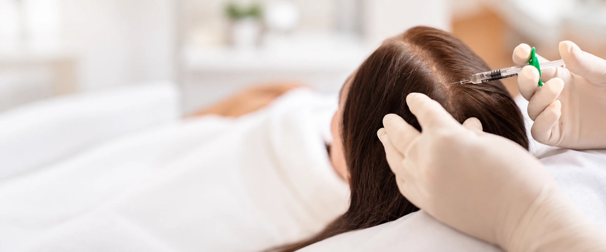 A medical professional wearing blue gloves administering a hair mesotherapy injection into a female patient's scalp to treat hair loss and promote hair growth in Dubai - Dr. Elham Keikha